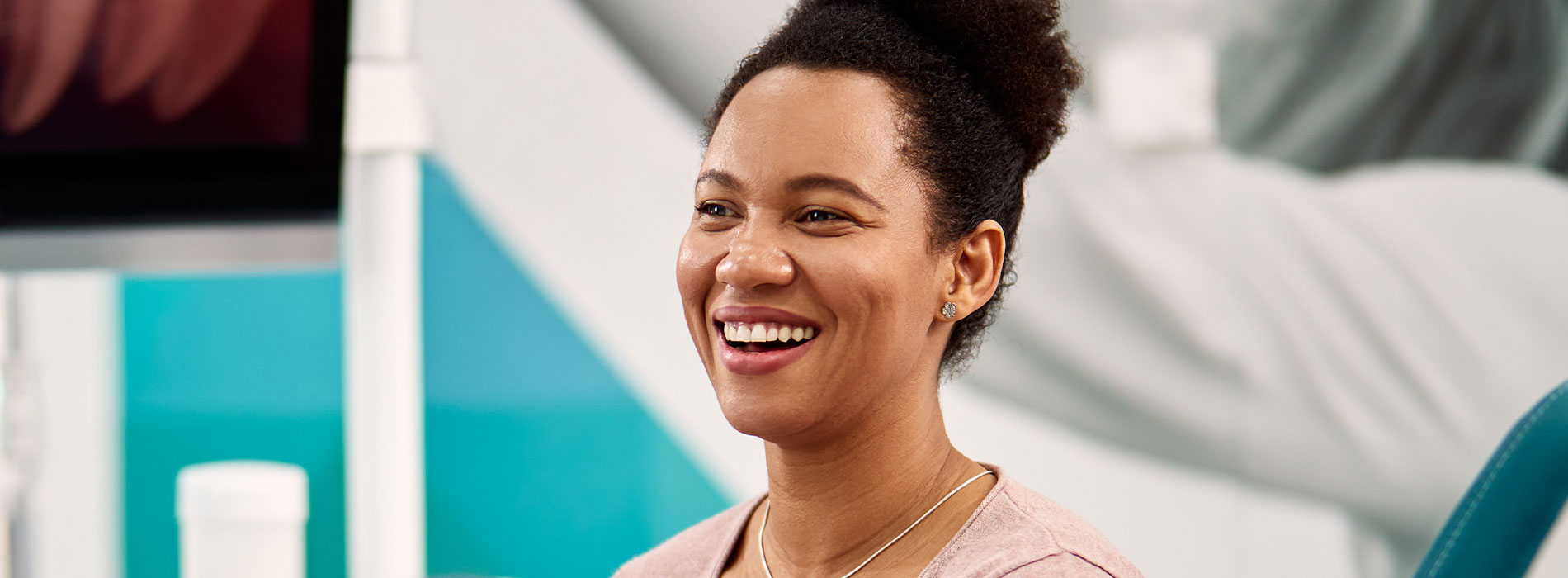 A person is seated in a dental chair, receiving care from a dental professional who stands behind them.